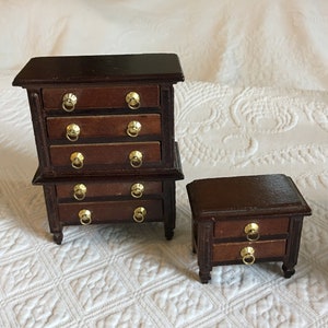 Könnte beinhalten: Ein Set aus zwei Miniatur-Kommoden aus Holz mit goldfarbenen Griffen. Die größere Kommode hat fünf Schubladen, die kleinere zwei.