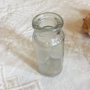 May include: A clear glass bottle with a textured surface. The bottle is empty and has a small opening at the top.