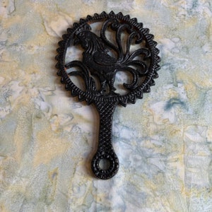 May include: Black cast iron hot pad shaped like a rooster with a decorative design.