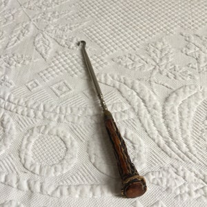 May include: A silver shoe horn with a brown antler handle. The handle has a decorative pattern.