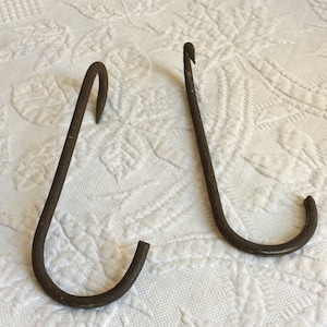 May include: Two rusty metal hooks with a curved shape. The hooks are on a white fabric background.