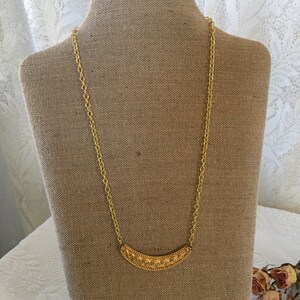 May include: A gold chain necklace with a decorative, curved pendant. The pendant has a detailed, swirling pattern.