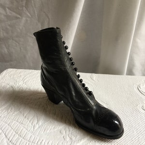 May include: A pair of black leather ankle boots with a button fastening up the front. The boots have a small heel and a rounded toe.
