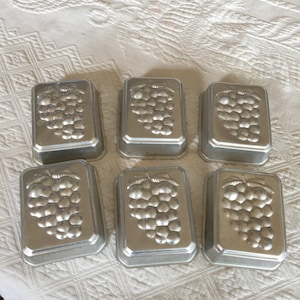 Könnte beinhalten: Sechs silberne, metallene Backformen in Traubenform. Die Formen sind rechteckig und haben ein erhabenes Design einer Traube.