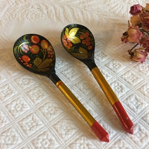 May include: Two wooden spoons with black and gold painted handles and red tips. The spoon bowls are painted with black, gold, red, and green floral designs.