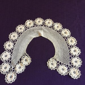 May include: White crocheted lace collar with a scalloped edge and floral designs.