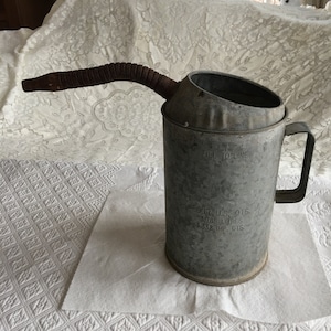 May include: A vintage galvanised metal oil can with a spout and handle. The can has a fill line and markings indicating it holds four UK quarts, 3.785 litres, and 3.332 imperial quarts.