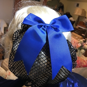 May include: A blue satin bow hair clip with a black mesh bun cover. The bow is tied in a large, classic bow shape.