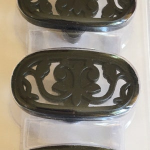 May include: Two black metal drawer pulls with an ornate floral design. The pulls are oval shaped and have a glossy finish.