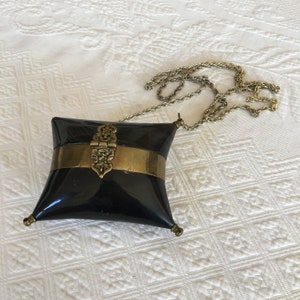 May include: A black, pillow-shaped purse with a gold chain strap and a gold clasp. The clasp has an ornate design.