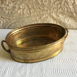 May include: Oval brass planter with two handles. The planter is empty and has a shiny finish.