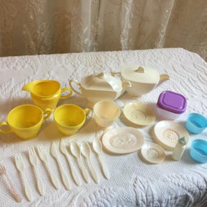 Puede incluir: Un juego de té vintage para niños con tazas, platillos, una tetera, una jarra de crema y un azucarero amarillos y blancos. El juego también incluye cucharas, tenedores y un cuchillo de plástico.