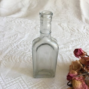 May include: A clear glass bottle with a square body and a narrow neck. The bottle is empty and has a slightly frosted appearance.