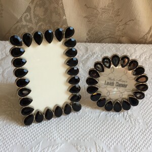 May include: A rectangular and a circular picture frame, both featuring a border of black, teardrop-shaped faceted stones set in a silver-toned metal frame. The circular frame contains a paper insert with the text Belle Maison Lavish Clamour 4x4.