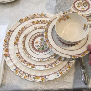 Puede incluir: Juego de vajilla vintage color crema con un estampado floral. Los platos y la taza de té presentan un borde festoneado y un diseño de flores amarillas y azules con detalles marrones. Un juego de té completo.