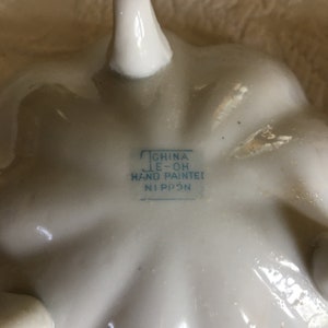 May include: Close-up of the bottom of a white ceramic dish with a blue stamp that reads "China E-Oh Hand Painted Nippon".