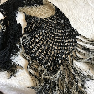 May include: Black crochet shawl with a fringe border. The shawl has a delicate, open-weave pattern and is made of soft, lightweight yarn.