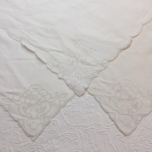 Könnte beinhalten: Weiße Vintage-Leinen-Taschentücher mit zarten, gestickten Blumenmustern in den Ecken. Die Taschentücher haben gewellte Kanten und sind auf einer strukturierten weißen Oberfläche angeordnet, die die filigrane Handarbeit und den klassischen Stil zeigt.