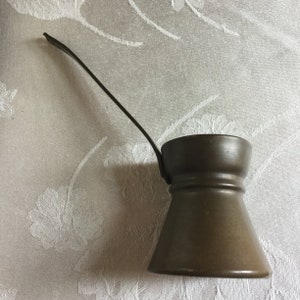 May include: A brown metal coffee pot with a long handle. The pot has a rounded base and a narrow neck.