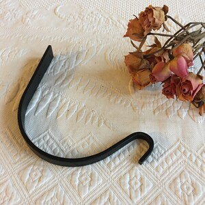 May include: Black metal hook with a curved design. The hook is attached to a flat metal plate.