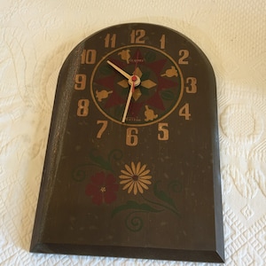 May include: A vintage brown wooden clock with a decorative floral design and gold numerals. The clock face features a starburst pattern with red and gold accents. The clock hands are gold and the clock reads "Setton Quartz".