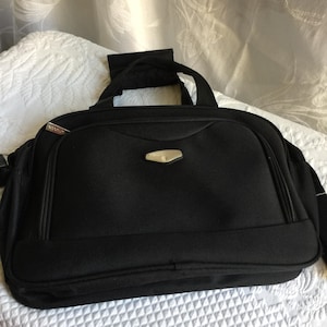 Puede incluir: Una bolsa de viaje negra con una cremallera plateada y un logotipo plateado que dice "Protec" en la parte delantera.