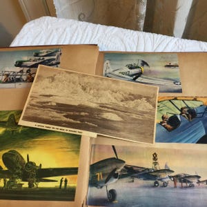 May include: A vintage scrapbook filled with photos of airplanes. The scrapbook includes a black and white photo of a crystal forest on the brink of Niagara Falls, a color photo of a blue and white airplane with the text "29117" on the side, and a color photo of a blue and white airplane with a pilot and co-pilot in the cockpit.