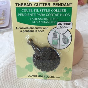 May include: Antique gold thread cutter pendant with a floral design. The packaging says "Thread Cutter Pendant" and "Coupe-Fil Style Collier".