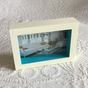 May include: White picture frame with a blue inner border. The frame is labeled "storehouse" and "4x6".
