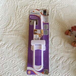 May include: Pack of two white plastic sliding locks for child safety. The packaging is purple and features the text "Dreambaby" and "Sliding Locks".
