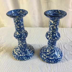 Op de afbeelding: Een paar bijpassende kandelaars met een blauw en wit gespikkeld patroon. Elke kandelaar heeft een brede ronde voet, een bolvormig middengedeelte en een uitlopende bovenrand die is ontworpen voor een standaard dinerkaars.