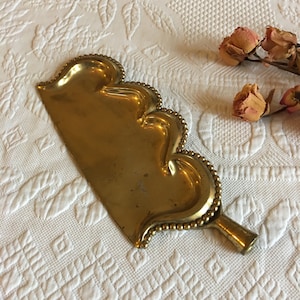 May include: A gold-colored metal dustpan with a scalloped edge and a beaded handle.