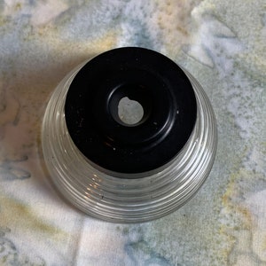 May include: A clear glass bottle with a black lid and a ribbed design. The bottle has a small hole in the lid.