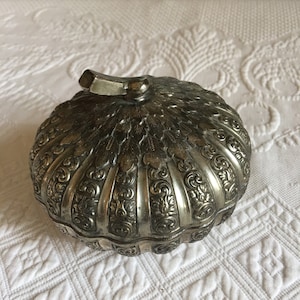 Może przedstawiać: Srebrna, ozdobna, dekoracyjna skrzynka w kształcie dyni z pokrywką na zawiasach. Skrzynka ma szczegółowy, tłoczony wzór z motywami kwiatowymi i liści.