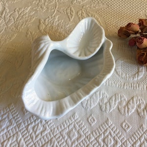 May include: A white ceramic seashell dish with two compartments. The dish is shaped like a clam shell with a smaller shell on top.
