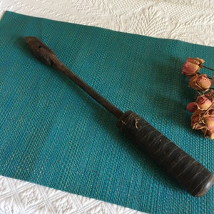 May include: A vintage soldering iron with a wooden handle and a metal tip. The iron is lying on a teal blue mat.