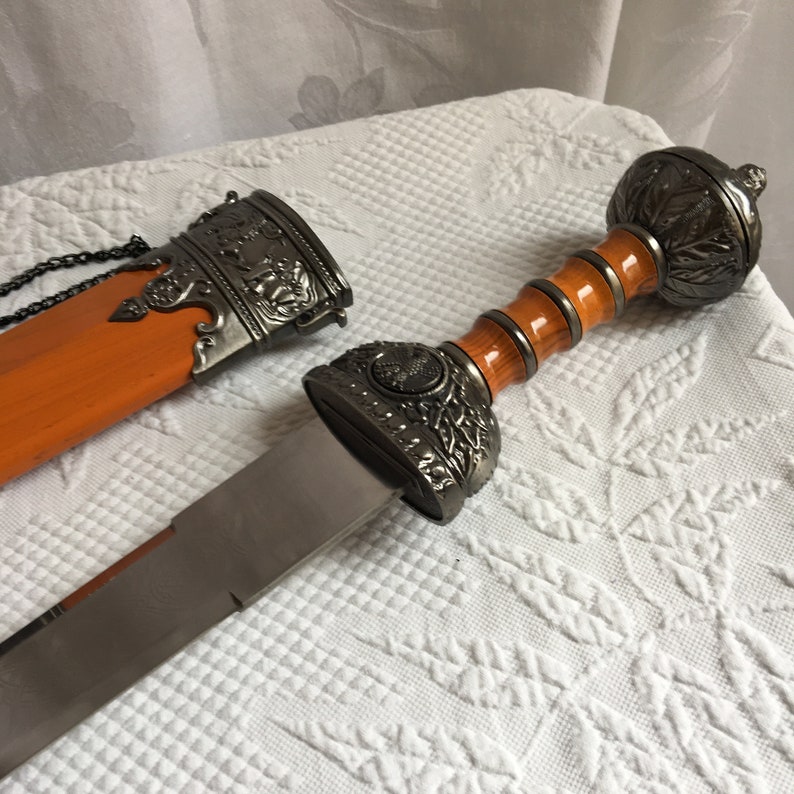 Puede incluir: Una espada de estilo romano en plata y marr&oacute;n con un mango y una vaina decorativos.
