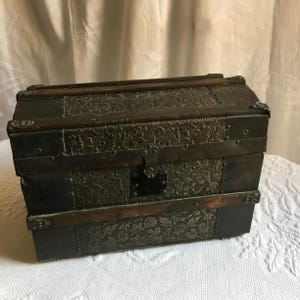 Antique Salesmans Sample Mini Steamer Trunk, koepelvormige bovenkant, gebosseleerde tinnen zijkanten, beschermende gespijkerde metalen randen en houten strips. Gevoerd met plank.