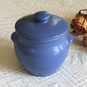 May include: A small, blue ceramic jar with a lid. The jar has two small handles on the sides.