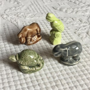 May include: A set of four small ceramic figurines of animals. The figurines are a brown and white zebra, a green parrot, a green turtle, and a gray elephant. The figurines are all in a standing position and are made of a glazed ceramic.