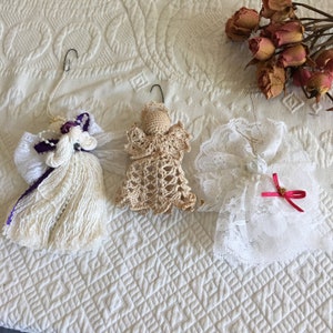May include: Three handmade crocheted angel ornaments, one white, one beige, and one white with lace trim. The ornaments are hanging from a white background.