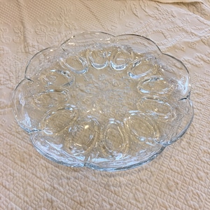 Peut inclure: Une assiette à œufs en verre transparent avec 12 indentations individuelles pour servir les œufs. L'assiette a un bord festonné et un motif décoratif.
