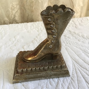 May include: A vintage metal boot shaped trinket holder. The boot is silver in colour with a decorative design on the top and a textured base.