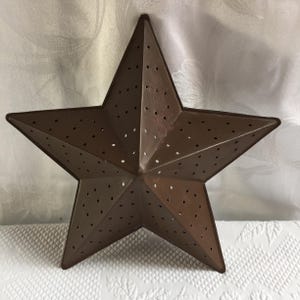 May include: A rustic, brown metal star with a five-point design. The star has numerous small, evenly spaced holes throughout its surface. This decorative star is likely used for home decor and adds a touch of country charm.