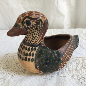 May include: A hand-painted ceramic duck planter with brown, green, and white accents. The duck has a wide, open beak and a detailed design.