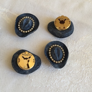 Puede incluir: Cuatro botones en forma de sombrero de vaquero azul y dorado con detalles de pedrería.
