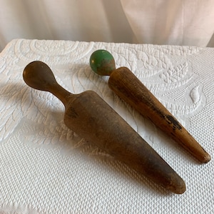 May include: Two wooden rolling pins, one with a green painted ball on the end. Both are tapered and have a worn, rustic look.