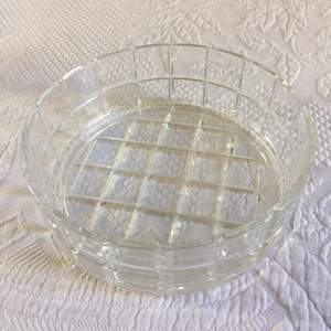 Puede incluir: Un cuenco redondo de vidrio transparente con un patrón de rejilla. El cuenco tiene un borde grueso y un patrón texturizado en forma de diamante en la base. El cuenco está sobre una superficie blanca estampada.