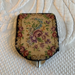 May include: A vintage floral embroidered compact with a black metal frame and a silver clasp.
