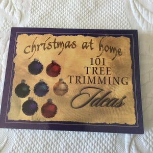 Puede incluir: Una portada de libro con un fondo vintage que presenta adornos y el texto "christmas at home 101 TREE TRIMMING Ideas".